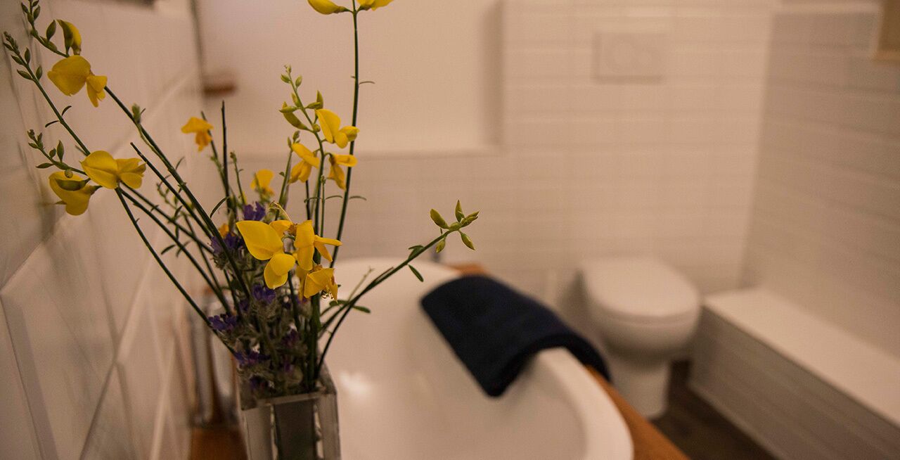 Une salle de bain avec une baignoire blanche, une serviette bleue et un vase rempli de fleurs jaunes.