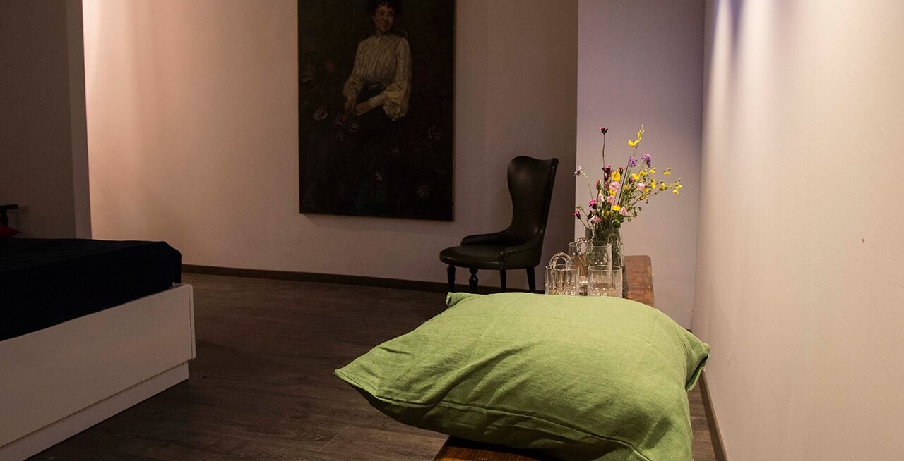 Una habitación con una cama, una silla, un cuadro en la pared y un florero con flores.