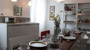 A modern kitchen with white cabinetry, a dining table set with plates, glasses, and a vase of flowers. - Residenza la Corte Assisi (Assisi)