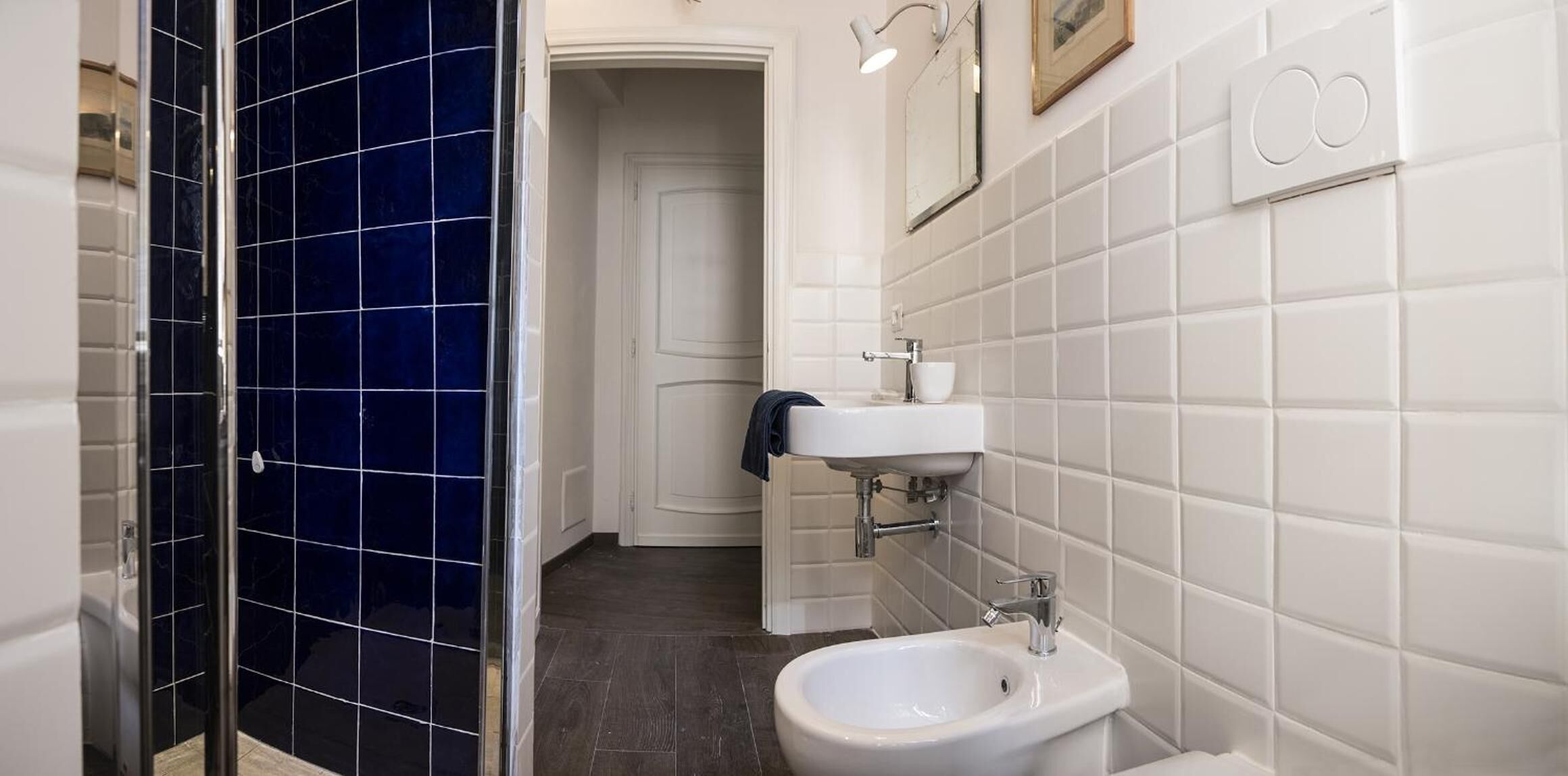 A bathroom with a white sink, a bidet, and a shower with dark blue tiles.