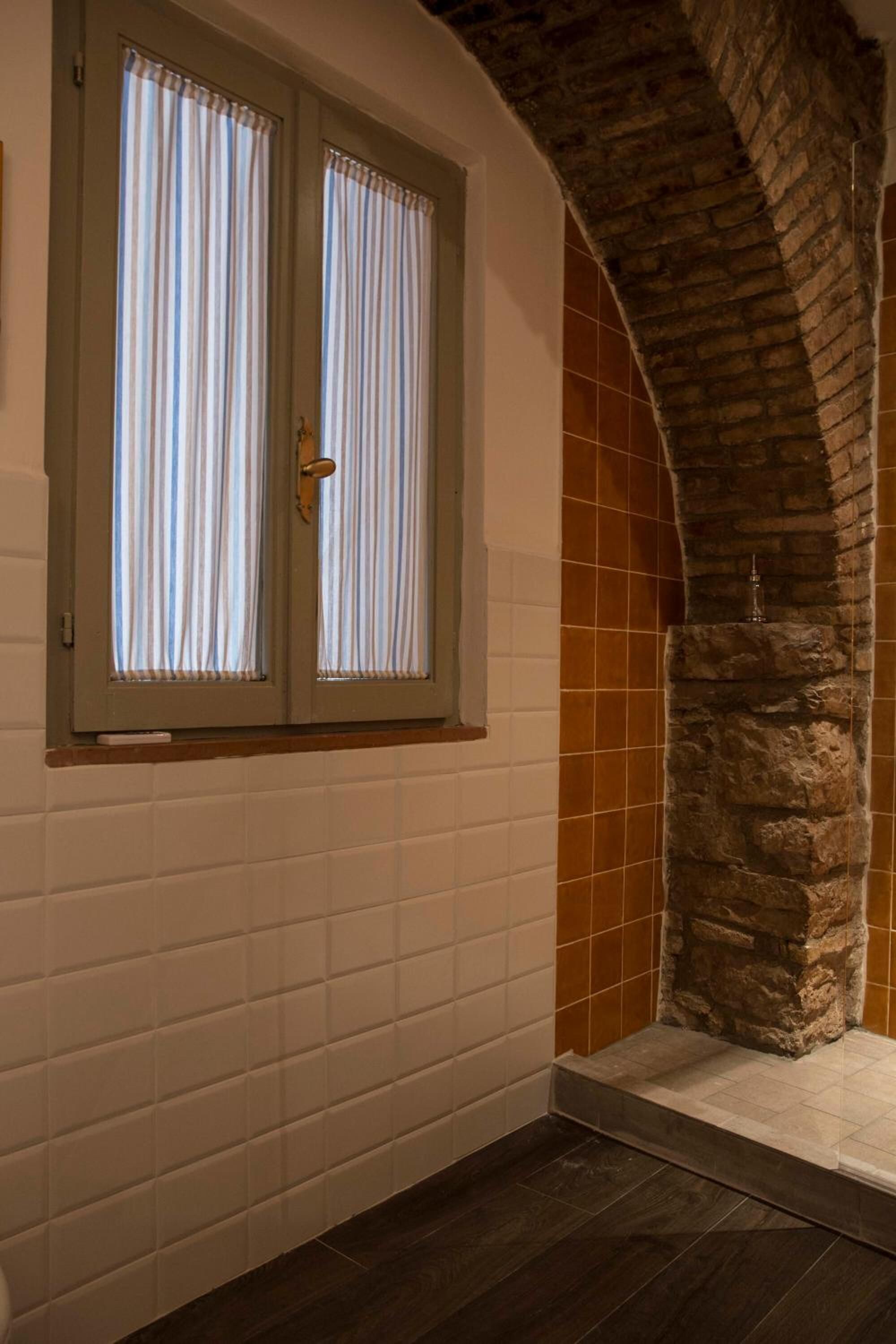 A room with a stone archway, a window with curtains, and a tiled wall.
