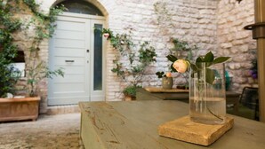 A rustic stone wall, a wooden table with a vase of flowers, and a door in the background. - Residenza la Corte Assisi (Assisi)