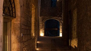 A narrow stone corridor with a door at the end, illuminated by a single light source. - Residenza la Corte Assisi (Assisi)