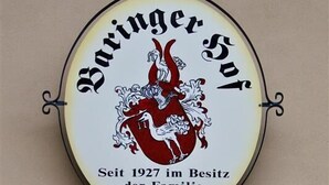 A circular sign with a red and white coat of arms and the text "Baringer Hof Seit 1927 im Besitz der Familie Dollinger". Below the sign, there is a framed plaque with the text "1712 PH". - Baringer Hof (Neuburg)