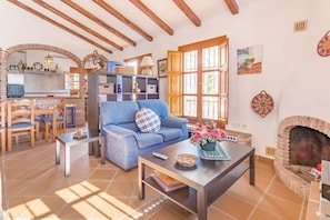 Una sala de estar con un sofá, una mesa de centro y una chimenea. Hay una zona de cocina con una ventana y una mesa de comedor con sillas.
