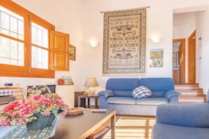 Una sala de estar con un sofá, una mesa con un cesto de flores y un tapiz colgado en la pared.