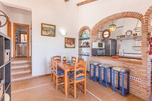 Un comedor con mesa y sillas de madera, una cocina con arco de ladrillo y una escalera que lleva a otra habitación.