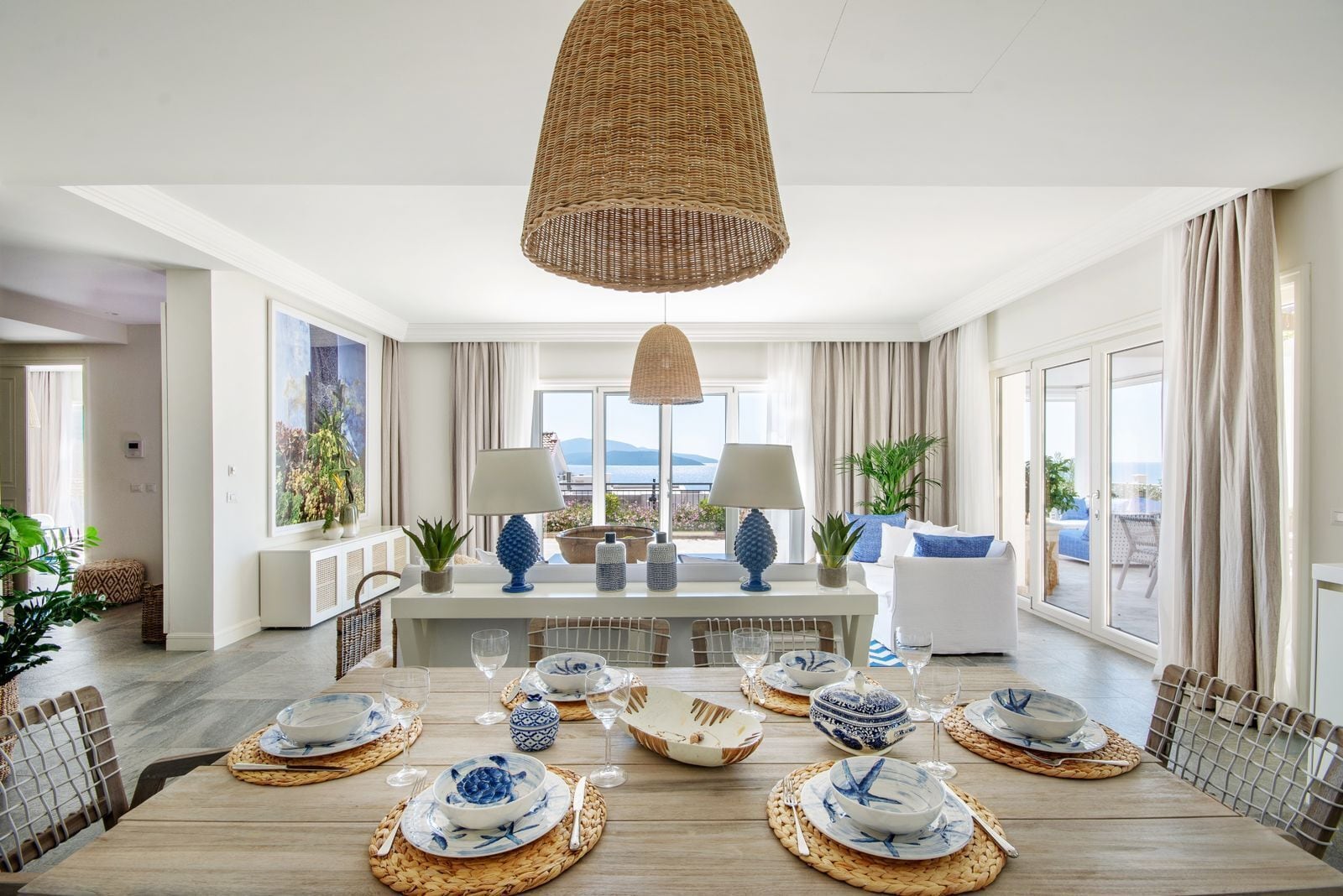Un vaste espace de salle à manger avec un plafond haut, un îlot central agrémenté d’une lampe, et une vue sur la mer grâce à de grandes fenêtres.