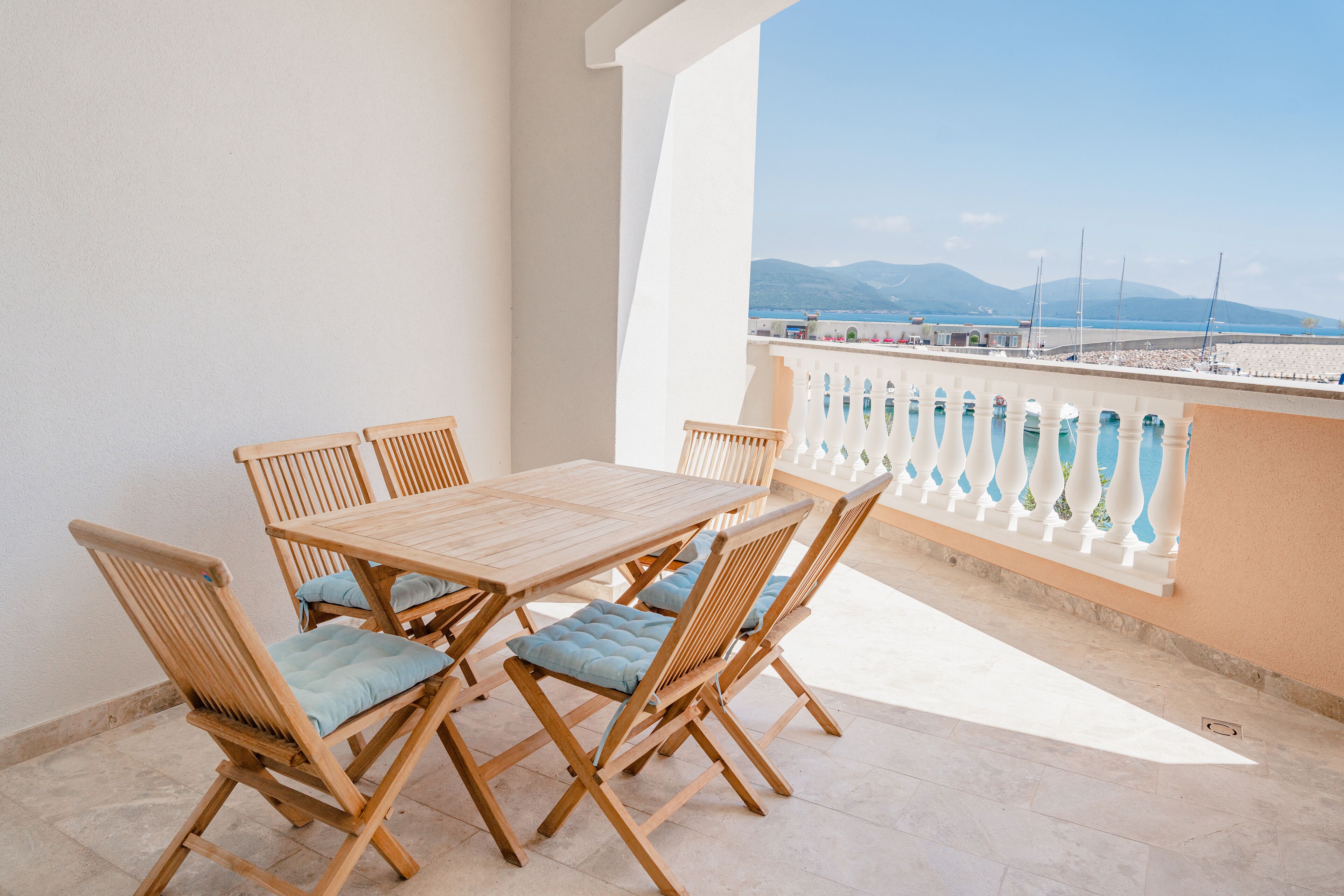A wooden table and chairs on a balcony with a view of the sea and mountains.