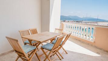 A wooden table and chairs on a balcony with a view of the sea and mountains.
