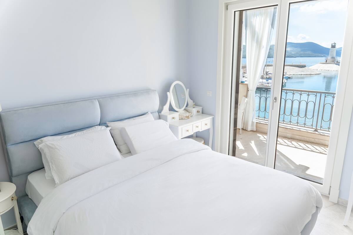 Ein Schlafzimmer mit einem großen Bett, einem Nachttisch, einer Kommode und Blick auf eine Küstenlandschaft mit einem Leuchtturm.