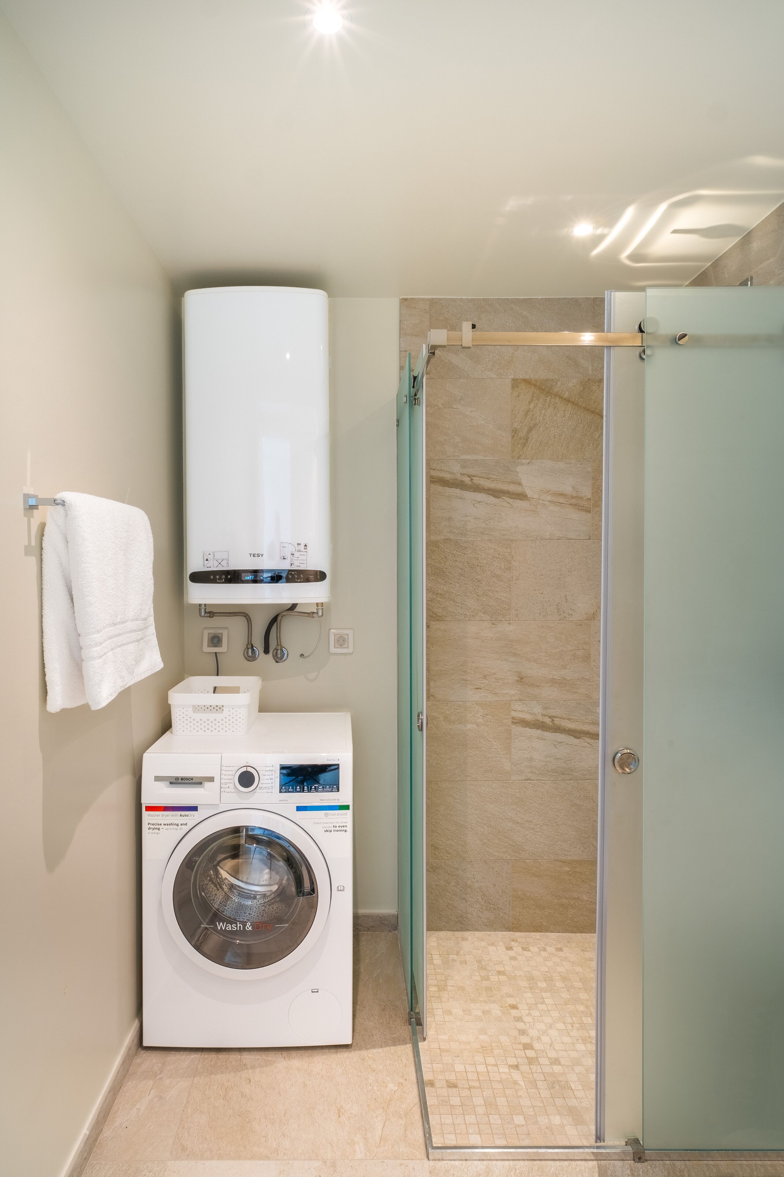 Un baño pequeño con lavadora, cabina de ducha de vidrio y toallero.