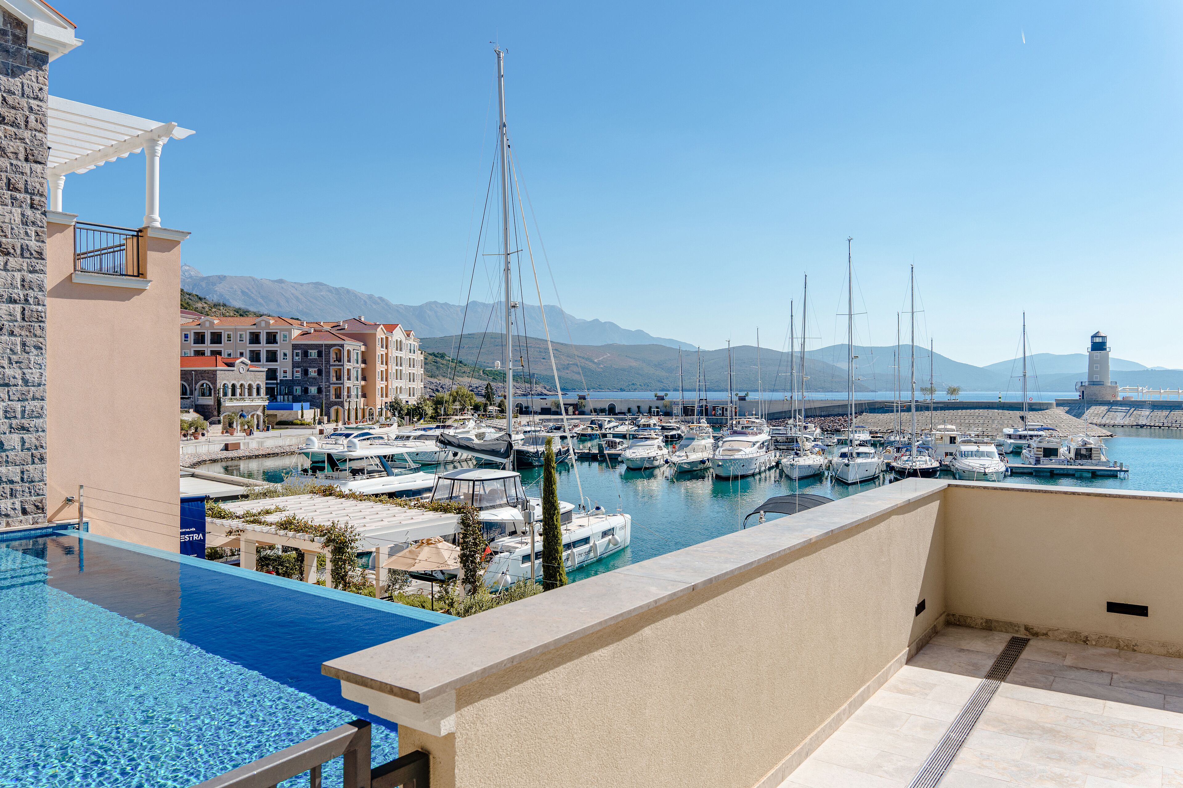 A marina with boats docked, a clear sky, and mountains in the background.