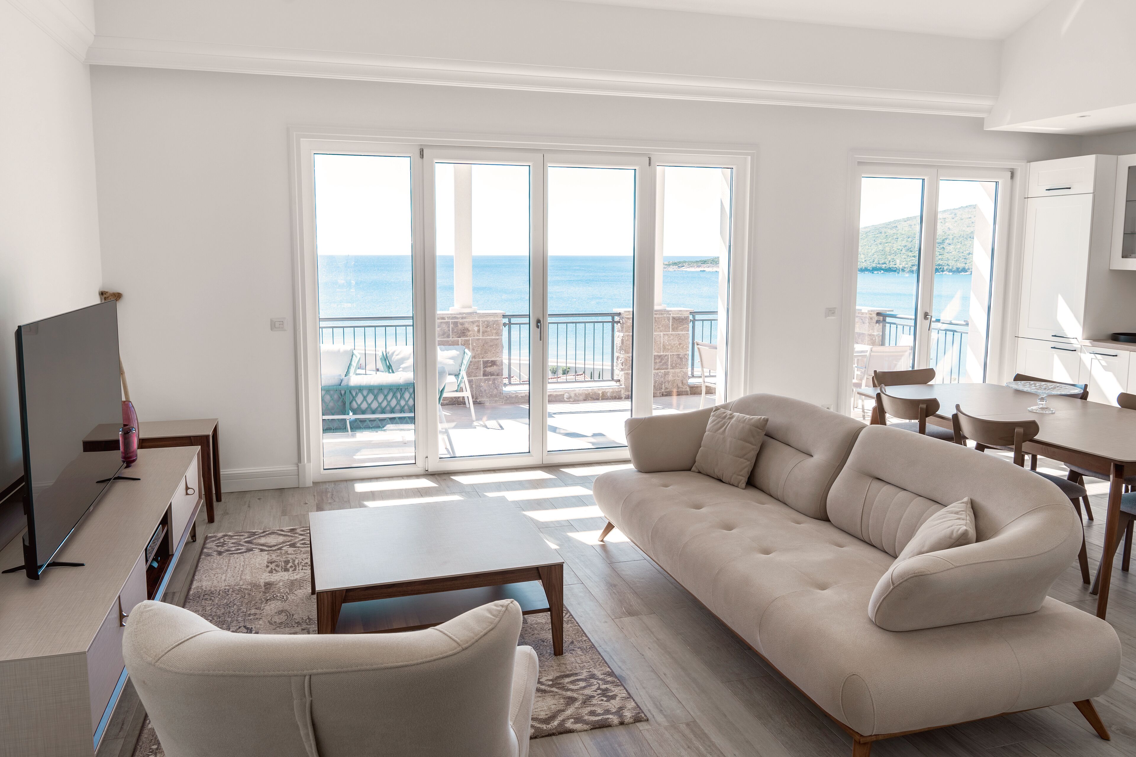A modern living room with a sofa, coffee table, TV, and a balcony with a view of the sea.