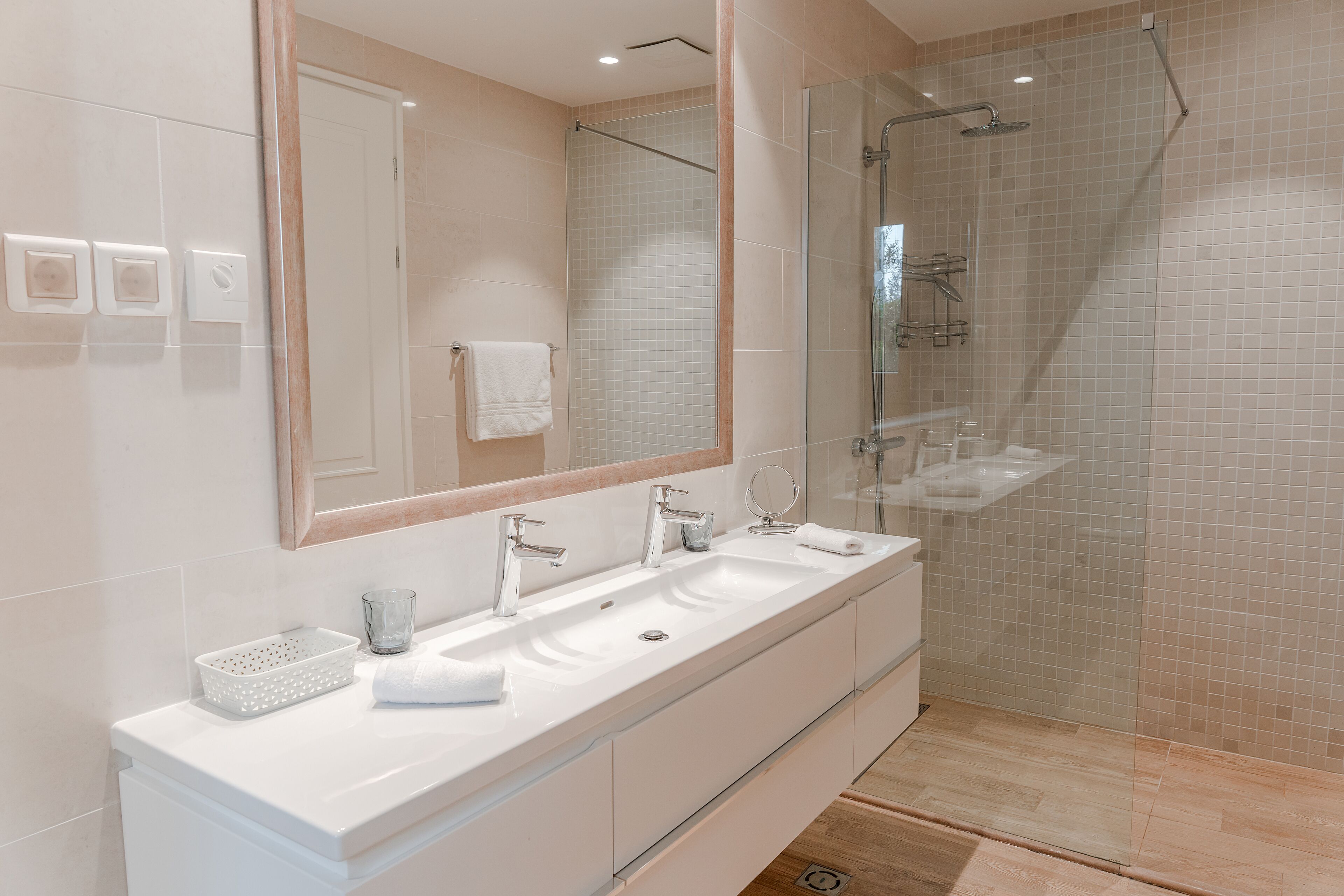 Un baño moderno con un espejo grande, dos lavabos y una ducha con cerramiento de vidrio.