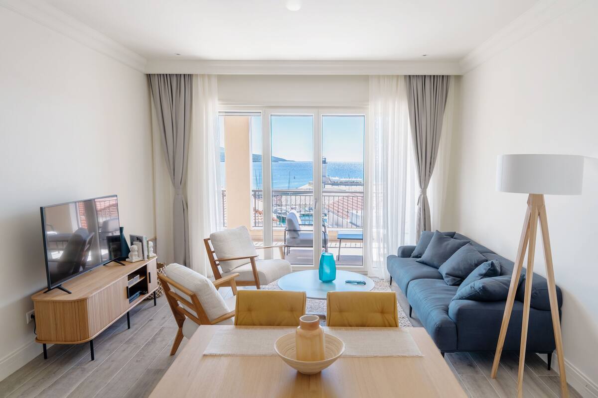 Ein modernes Wohnzimmer mit Fernseher, Sofa, Esstisch und Meerblick durch große Fenster.