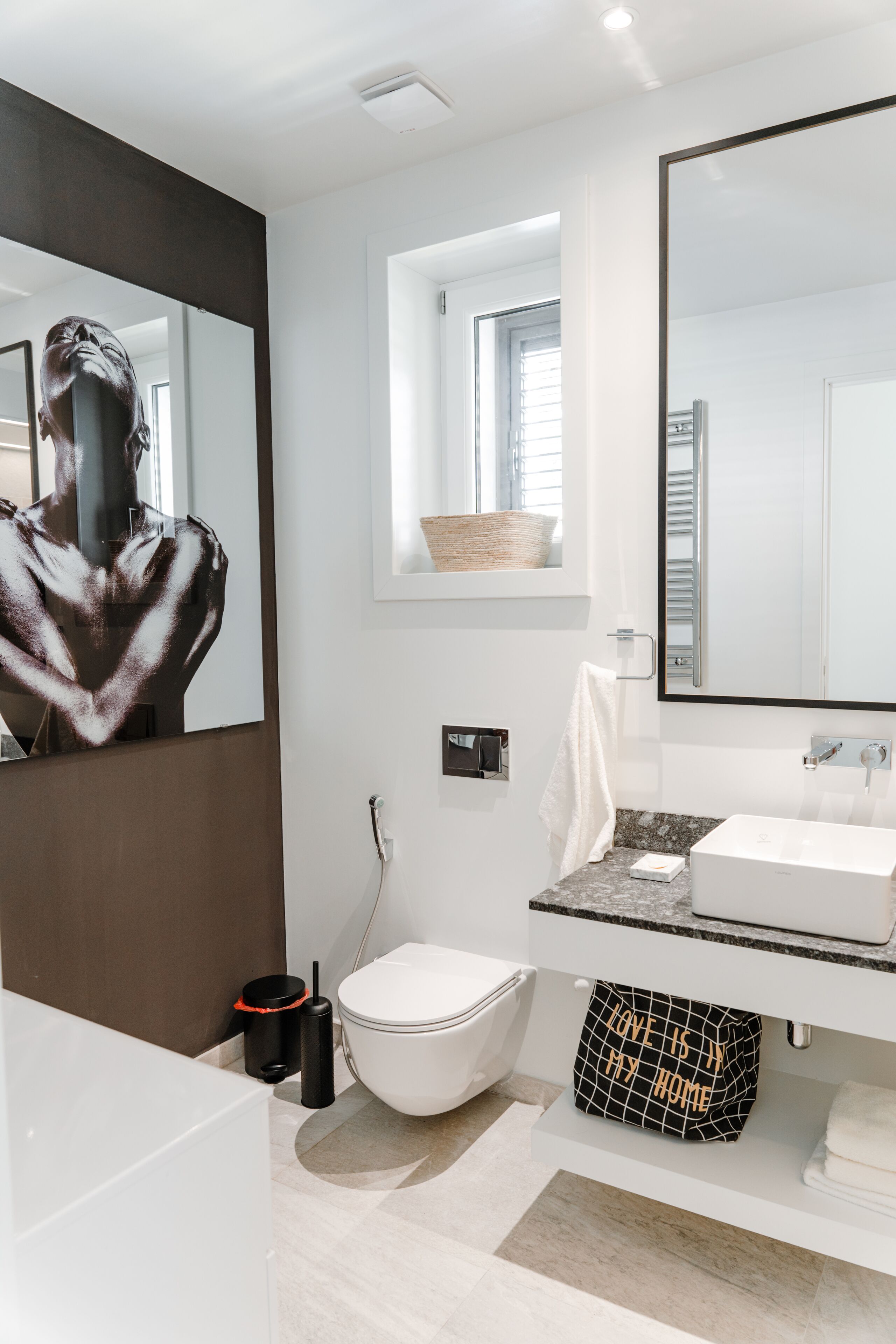 A modern bathroom with a large mirror, white fixtures, a towel rack, and a small window.