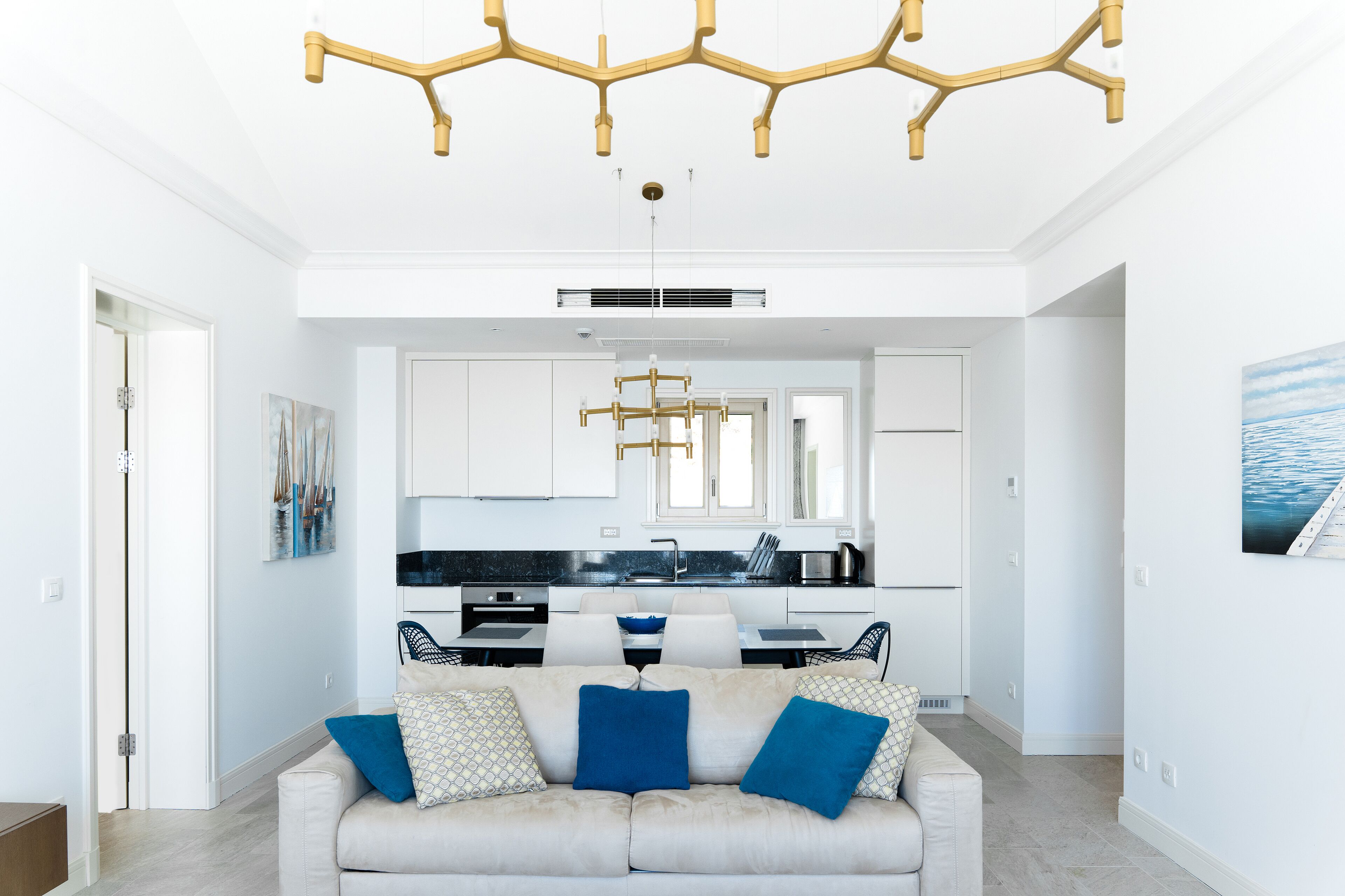 Ein stilvolles Wohnzimmer mit einem beigefarbenen Sofa, blauen Kissen und einer einzigartigen Gold-Kronleuchter.
