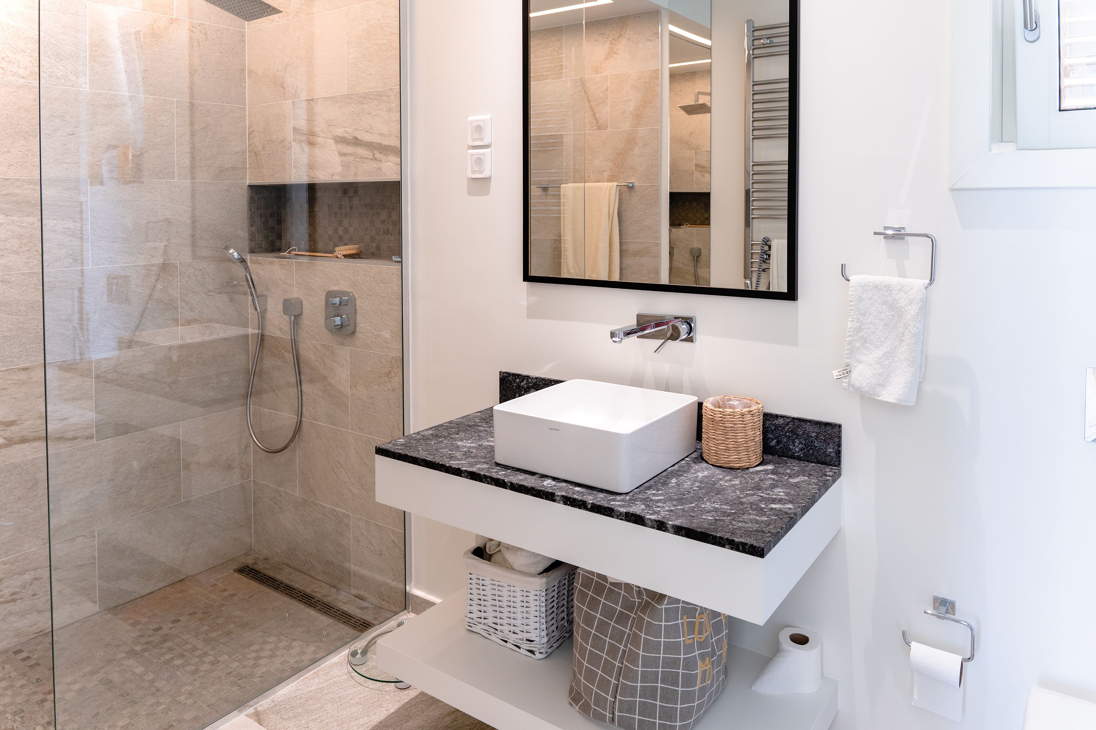 A modern bathroom with a glass-enclosed shower, a white sink with a marble countertop, and a large mirror above the sink.