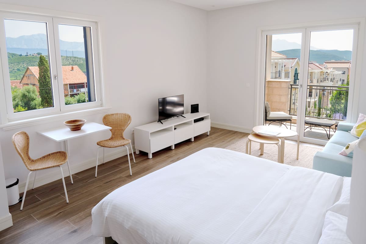 Ein modernes Hotelzimmer mit einem großen Bett, einem Fernseher, einem Esstisch und einem Balkon mit Blick auf Stadt und Berge.