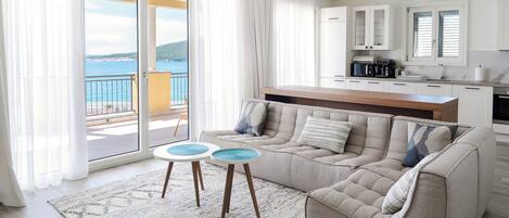 A modern living room with a sofa, two side tables, and a view of the sea through large windows.