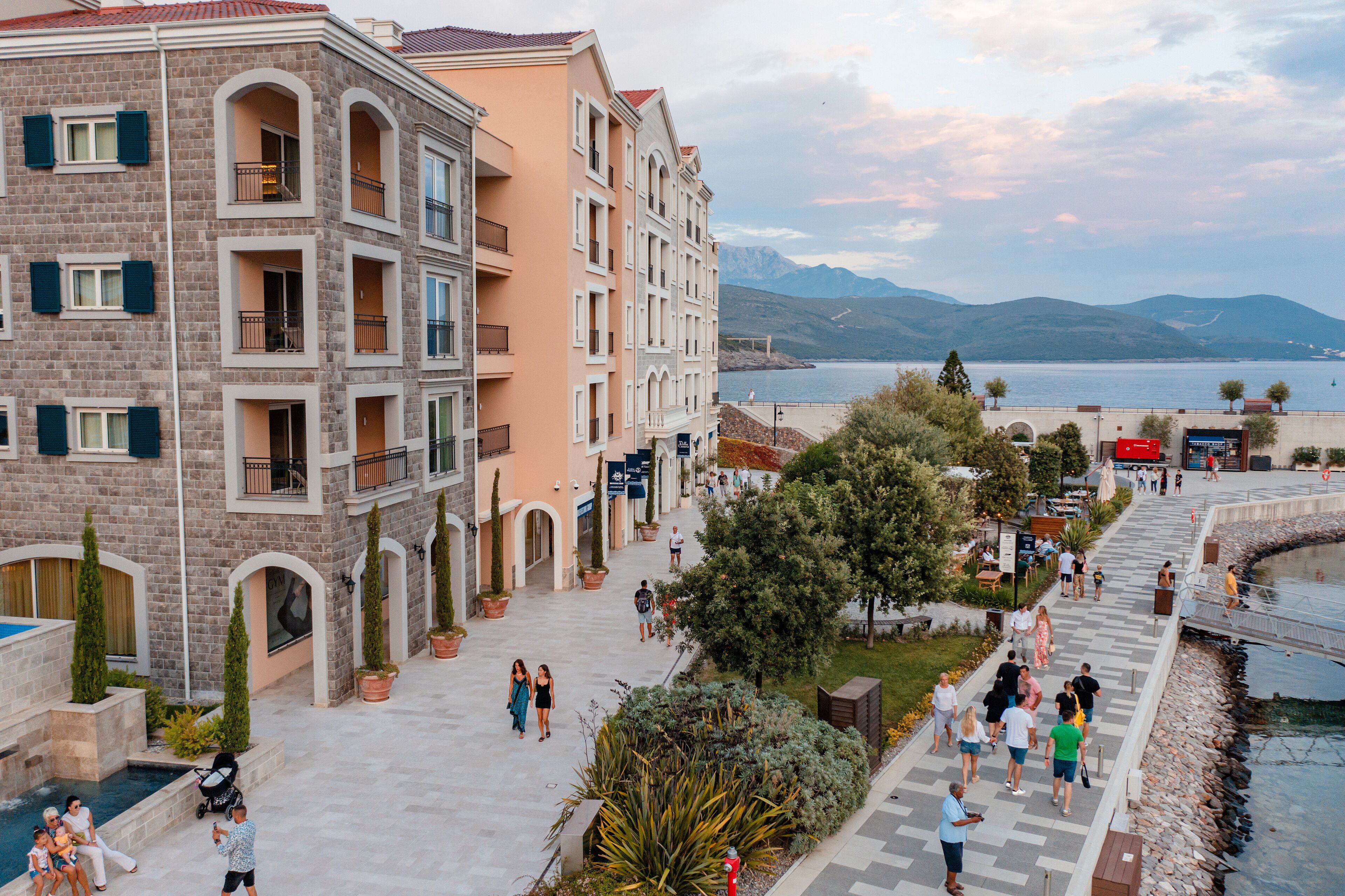 A multi-story building with balconies, a swimming pool, and a waterfront promenade.