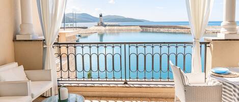 A balcony with a view of a body of water, a lighthouse, and mountains in the distance.