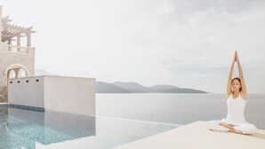 Una persona meditant al costat d'una piscina amb vista al mar i a les muntanyes.