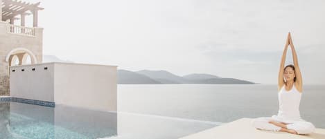 A person meditating by a pool with a view of the sea and mountains.