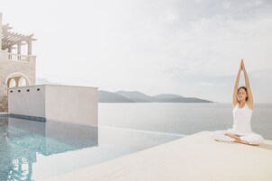 Uma pessoa meditando junto a uma piscina, com vista para o mar e montanhas.