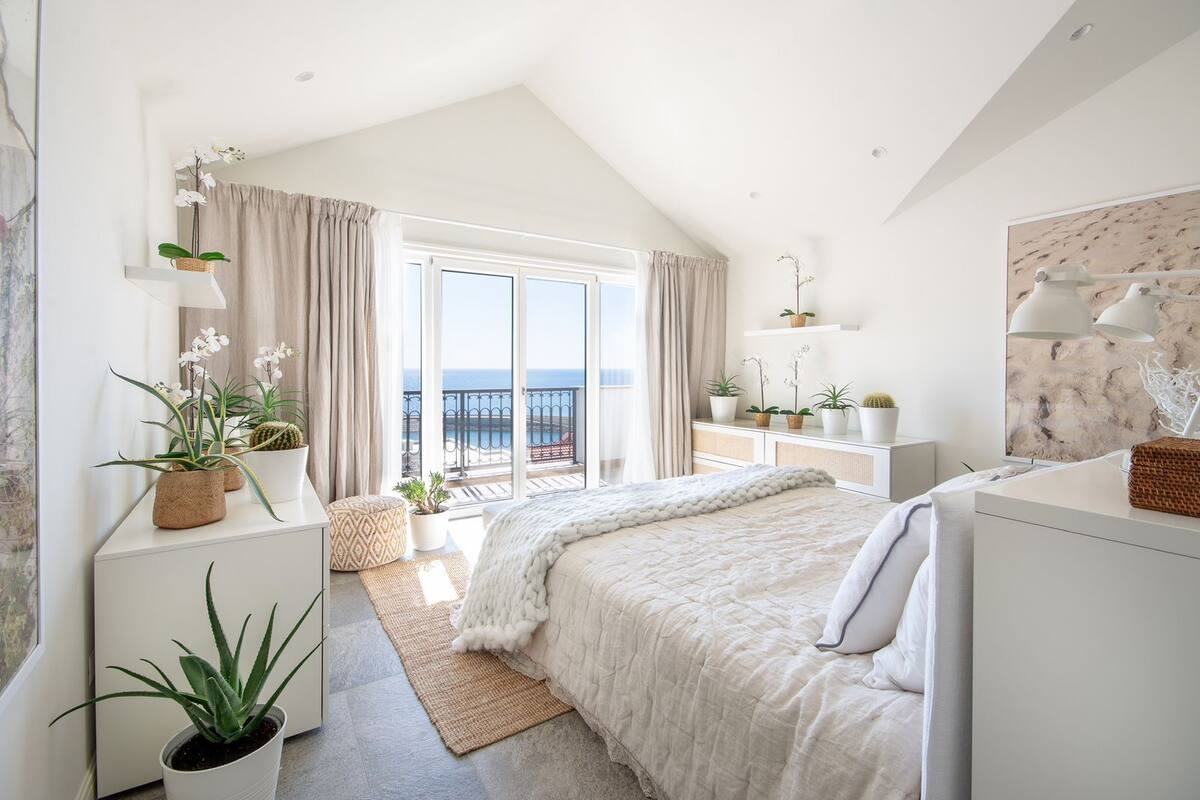 Ein modernes Schlafzimmer mit einem großen Bett, einem Balkon mit Pflanzen und Meerblick.
