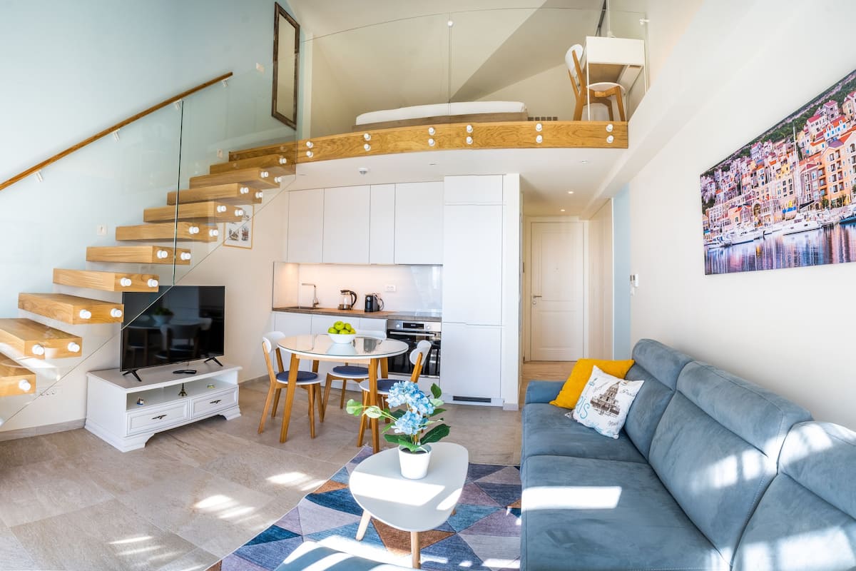 Eine moderne Wohnung mit Wendeltreppe, einem Wohnzimmer mit Sofa und Fernseher, einem Essbereich und einer Küche.