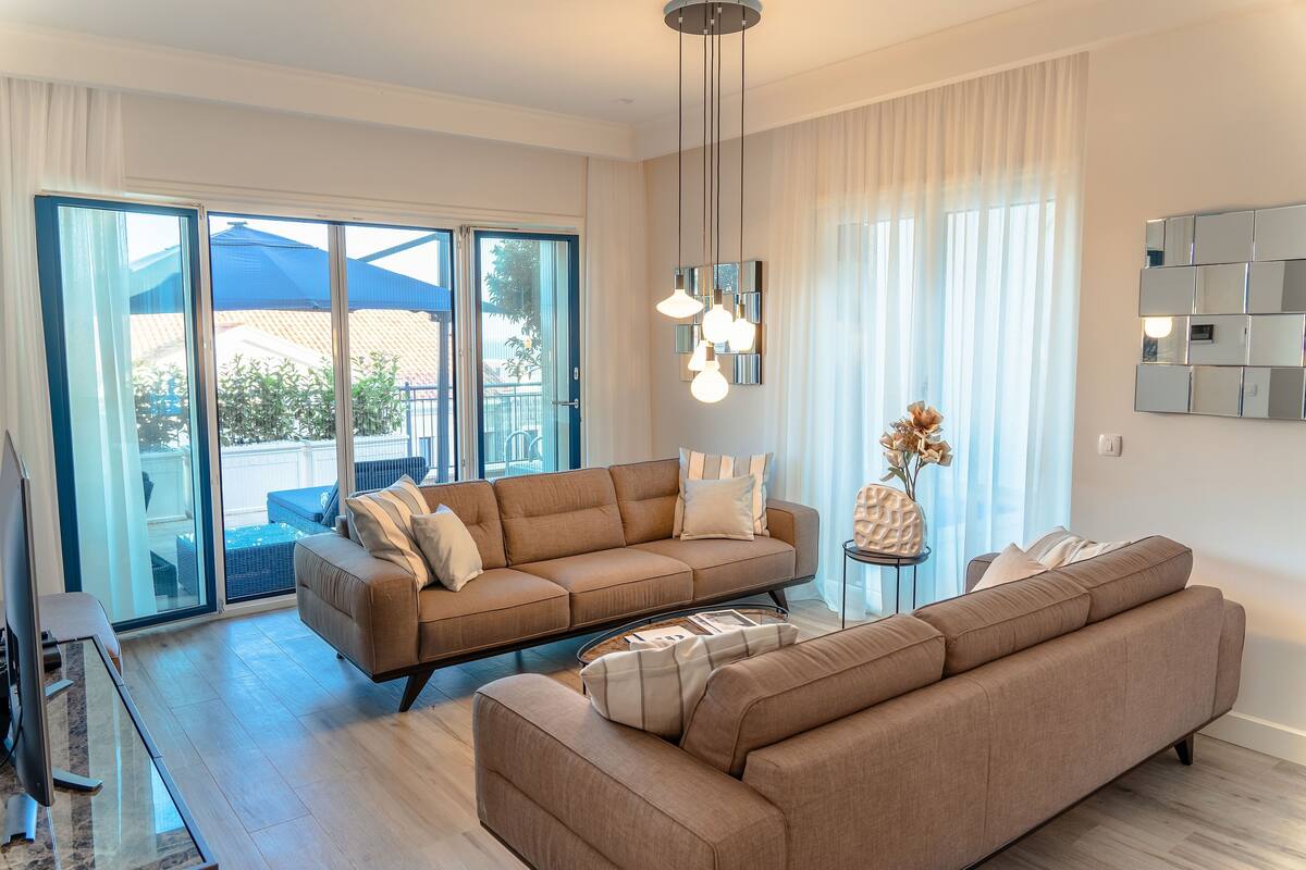Ein modernes Wohnzimmer mit einer Couch, einem Couchtisch und einem Klavier. Ein großes Fenster mit Vorhängen bietet einen Blick nach draußen.