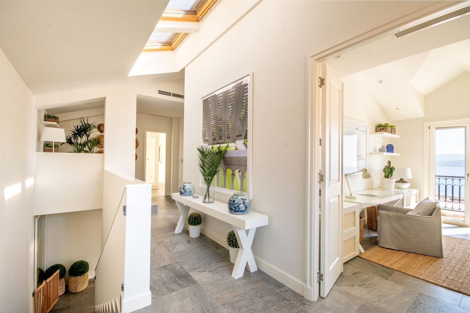 A modern interior with a staircase, a white console table with decorative items, and a view of the outdoors through a door.