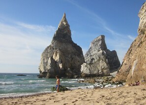A beach with rocky formations and a person standing on the sand.