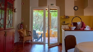 Une pièce dotée d'une porte-fenêtre coulissante donnant sur un espace extérieur, d'un fauteuil en osier, d'une table avec un panier et d'une horloge au mur.