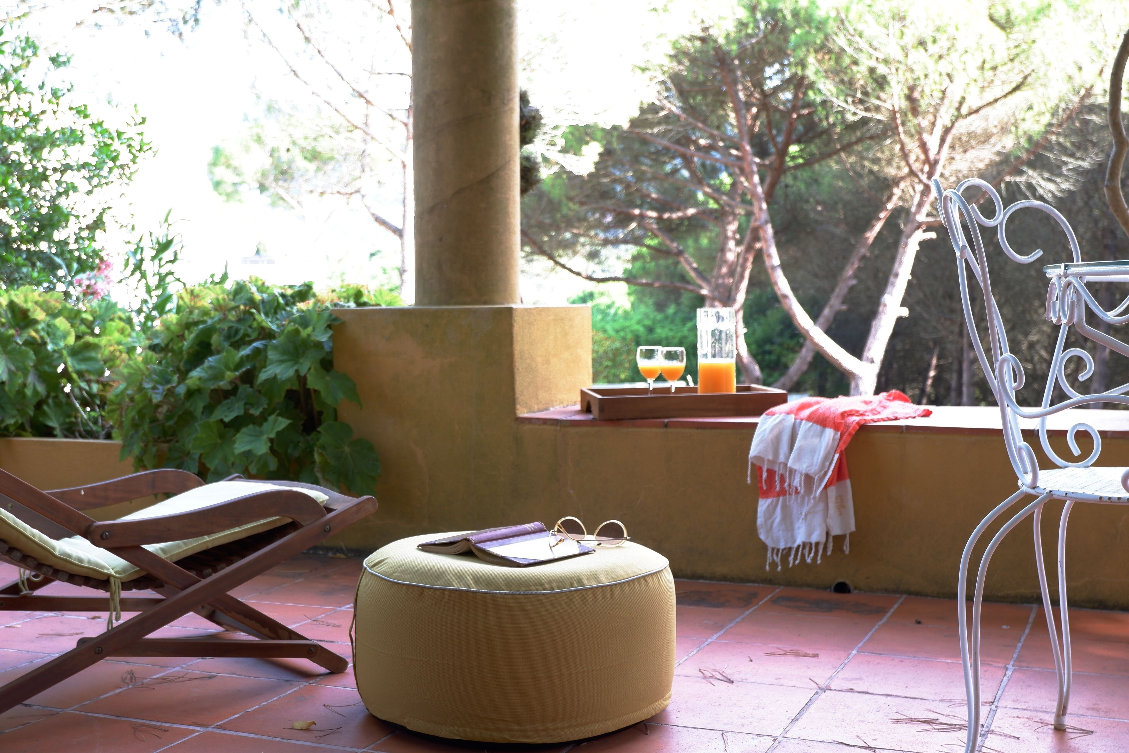 Un patio con una silla de lounge de madera, una silla metálica blanca y un otomano redondo.