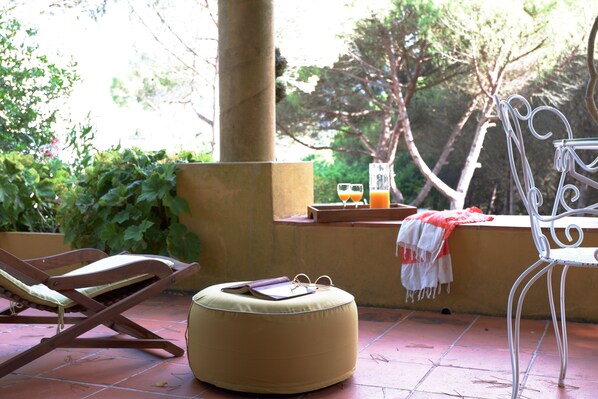 A patio with a wooden lounge chair, a white metal chair, and a round ottoman.
