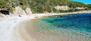 Una platja amb aigua cristal·lina, roques i un turó boscós.