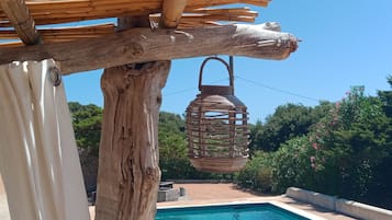Un espace piscine agrémenté d’un panier suspendu en osier, d’une pergola en bois et offrant une vue sur la verdure.