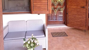 Un patio couvert avec un canapé en osier, une plante en pot et des portes en bois.