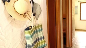 Un couloir où se trouve un porte-chapeaux sur lequel est posé un chapeau de paille et un sac en osier.
