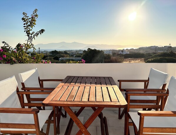 A wooden table and chairs on a balcony with a view of mountains and a cityscape.