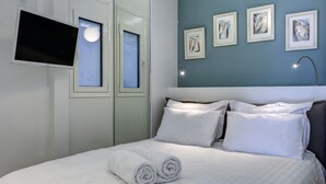A neatly made bed with white linens and pillows, a flat-screen TV mounted on the wall, and three framed pictures on the wall. - Frixos Acropolis luxury apartment (Athens)