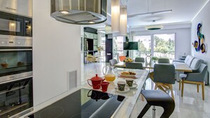 A modern kitchen with stainless steel appliances, a glass dining table with chairs, and a view of the outdoors through large windows. - Frixos Acropolis luxury apartment (Athens)