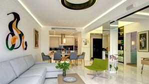 A modern living room with a grey sofa, a coffee table, and a green chair. There is a dining area with a table and chairs in the background. - Frixos Acropolis luxury apartment (Athens)