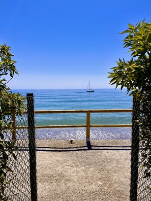 A beach view with a fence, a sailboat, and clear blue sky.