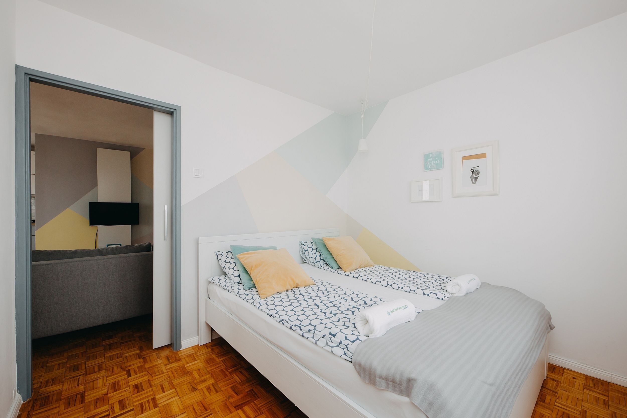 A bedroom with a bed, a sofa, and a desk. There are two framed pictures on the wall.
