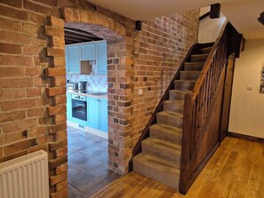 A staircase with wooden railings leading to a kitchen area with blue cabinets and a brick wall.