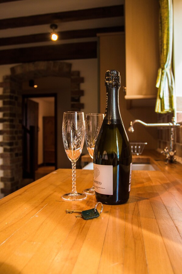 A bottle of wine and two glasses on a wooden table in a room with brick walls and a stone archway.